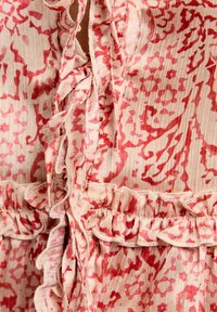 Top in tessuto con motivo floreale in un morbido rosa con accenti rossi, caratterizzato da bordi arricciati, lacci al colletto e superficie testurizzata.