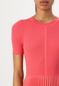 Abito rosa a coste con maniche corte, dotato di un top aderente e di una gonna plissettata. Tessuto morbido con scollatura rotonda e cuciture verticali.
