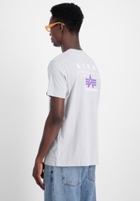 Hallus halli puuvillane T-särk lühikeste varrukatega, millel on seljal lilla graafiline logo. Disain sisaldab ümmargust kaelust ja sirget allserva.