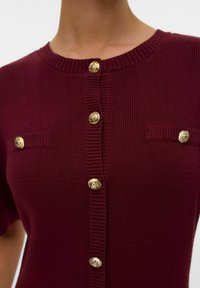 Cardigan a maglia corto bordeaux a maniche corte con texture a coste, bottoni decorativi dorati e due tasche con accenti di bottone abbinati.