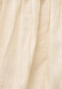Linen fabric in a soft cream color with a smooth, slightly translucent texture, featuring natural wrinkles and draping folds.