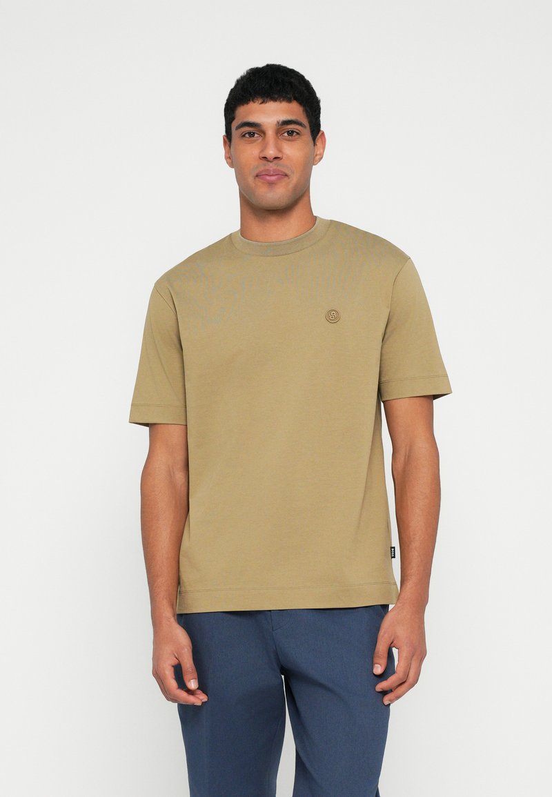Oliwkowa bawełniana koszulka z okrągłym dekoltem, krótkimi rękawami i małym logo na piersi. Charakteryzuje się prostym krojem i gładką fakturą.