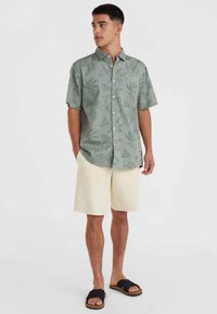 Korte mouwen, lichtgroen button-up shirt met een botanisch patroon, gecombineerd met crèmekleurige shorts en zwarte slippers.