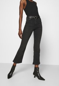 Jeans flare in denim nero con vita alta, abbinati a una cintura nera con accessori in argento e stivali neri con tacco all'altezza della caviglia.