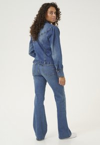 Denim jakna s napuhanim rukavima, modre barve in gumbi. Kombinirana s razširjenimi kavbojkami, obema v podobni pranji, z minimalnim šivanjem.