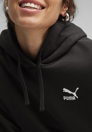 Sort hættejakke med snor, der har et hvidt Puma-logo. Glat tekstur, afslappet pasform og med kængurulomme.
