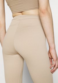 Beige ribbade tights med hög midja. Tyget är slätt och har vertikala ränder, och plaggstycket matchas med en kort topp.