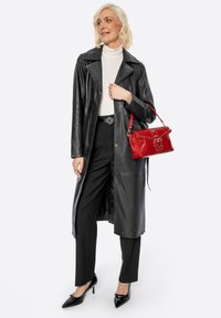 Černý kožený trenčkot s vykrojeným límcem, spárovaný s černými kalhotami. Červená kabelka s cvočky a sponou. Černé špičaté lodičky.