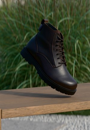 Bottine en cuir marron foncé avec des lacets flottant au-dessus d'une surface en bois, avec un feuillage vert flou en arrière-plan.