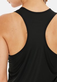Top da allenamento nero con design a schiena scoperta, realizzato in tessuto a coste, che mette in risalto la schiena e le spalle.