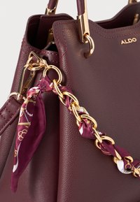 Sac à main en faux cuir bourgogne avec des accessoires en or, une bandoulière en chaîne décorative et un accent en foulard en soie noué. Finition texturée et design structuré.