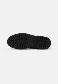 Suela de zapato de goma negra con profundos treads texturizados y una forma redondeada. Cuenta con un acabado suave y un área de talón reforzada.