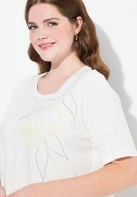 Hvid t-shirt med korte ærmer, der har broderede designs af citroner og blade i gul og grøn på fronten. Blødt stof med en afslappet pasform.