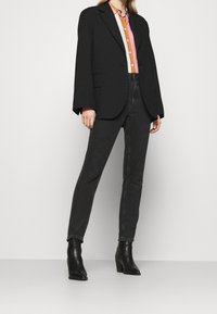 Svart oversized blazer, randig skjorta med knappar i orange och rosa, högmidjade svarta jeans och svarta klackstövlar.