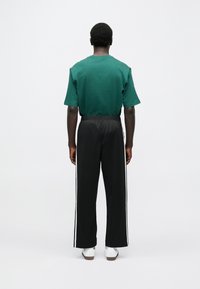 Πράσινο βαμβακερό t-shirt με κοντά μανίκια, συνδυασμένο με μαύρο φαρδύ παντελόνι φόρμας με λευκές πλαϊνές ρίγες και λευκά αθλητικά παπούτσια.