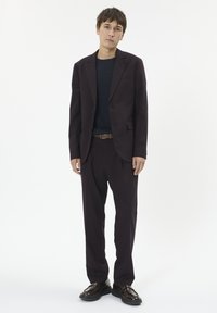 Costum croșetat vinovat cu sacou cu un singur rând de nasturi și pantaloni asortați. Purtați peste o cămașă bleu închis, asortați cu pantofi negri. Textură netedă.