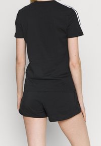 Svart atletisk t-shirt med korta ärmar och rak skärning, matchad med svarta shorts. Har vita accentremsor längs axlarna.