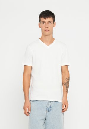 T-shirt bianca in cotone a V con maniche corte, caratterizzata da un design semplice e una vestibilità rilassata, indossata con pantaloni shorts in denim chiaro.