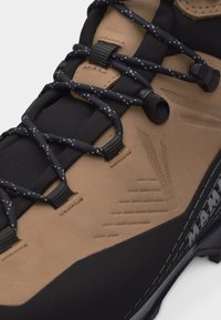 Καφέ ανοιχτό και μαύρο παπούτσι πεζοπορίας με κορδόνια σε μαύρο και λευκό που έχουν στίγματα, περασμένα μέσα από υφασμάτινες θηλιές και μεταλλικά κορδόνια.