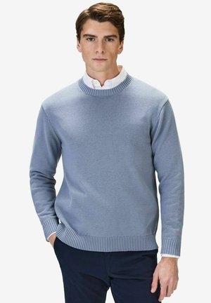 Lyseblå strikket sweater med ribbede manchetter og kant, rund halsudskæring og tekstureret stof, båret over en hvid skjorte med krave.