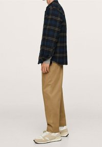 Camicia in flanella a quadri blu navy e nera, abbinata a pantaloni beige e sneakers beige. La camicia presenta un colletto con bottoni e maniche lunghe.