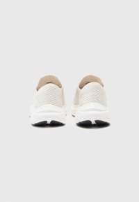 Baskets slip-on beiges avec une tige en maille texturée, un col rembourré et une semelle blanche amortissante avec un tread en caoutchouc noir.
