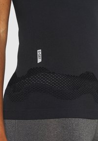 Top atlético negro con textura de malla en la cintura, que presenta un patrón de olas texturizado y un pequeño logo "B-DRY" en un costado.