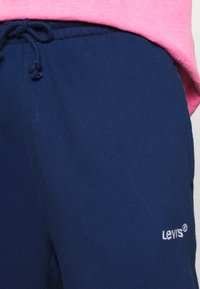 Tamno plave trenerke od mekog materijala, sa elastičnim pojasom i vezicom, na strani imaju bijeli izvezeni Levi's logo.