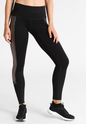Zwarte leggings met een hoge tailleband, voorzien van een gestructureerd zijpaneelontwerp in goud. Materiaal lijkt rekbaar en aansluitend.