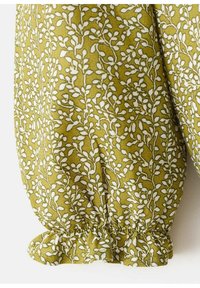 Zielony materiał z białym botanicznym nadrukiem, z małymi liśćmi. Dolny brzeg ma zgromadzony detal dla tekstury i kształtu.