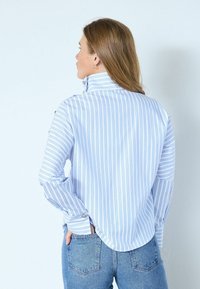 Blå och vitrandig blus med hög krage, långa ärmar och knappade manschetter, gjord av lätt tyg. Buren med högmidjade jeans.