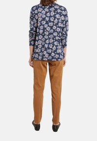 Top de manga larga floral en color azul marino con un corte holgado, combinado con pantalones beige. El conjunto presenta una mezcla de tejidos suaves y una textura lisa.