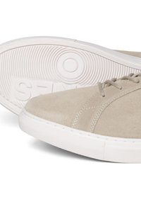 Zapatillas de ante beige con una suela de goma blanca lisa, que cuentan con cordones y costuras en tonos similares. Punta redondeada con un patrón texturizado en la suela.