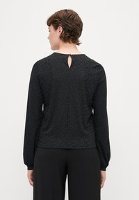 Blusa preta com um padrão de leopardo subtil, mangas longas e um recorte nas costas com fecho de botão. Tecido suave e silhueta ajustada.