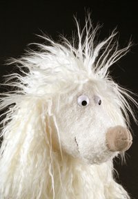 White furry toy with a round head, large googly eyes, a brown snout, and long, messy hair. Features a textured, fluffy surface.
