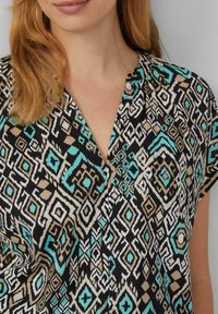 Zwarte en turkoois gestreepte blouse met korte mouwen, voorzien van geometrische ontwerpen in wit en bruin, zachte stof textuur en een V-hals.