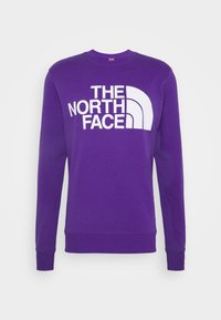 Fialová mikina s dlouhými rukávy, kulatým výstřihem a bílým logem "THE NORTH FACE". Má žebrované manžety a lem. Vyrobena z měkké látky.