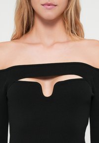 Μαύρη μπλούζα χωρίς ώμους από ριμπ ύφασμα, με V-shaped κοψίματα στο στήθος και φαρδύ λαιμό. Απαλή υφή, εφαρμοστή σχεδίαση.