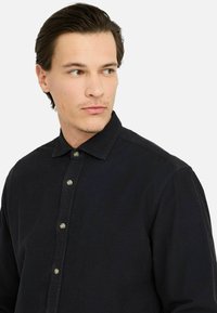 Camicia in corduroy blu scuro con colletto. Presenta cinque bottoni metallici sulla parte anteriore e una superficie texture.