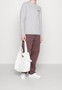 Maglione grigio a maniche lunghe, vestibilità rilassata, abbinato a pantaloni bordeaux. Borsa a tracolla bianca in tela con dettaglio del logo e sneaker bianche.