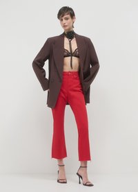 Braunes Doppelreiher-Sakko über einem schwarzen Spitzen-Bralette, kombiniert mit hoch taillierten roten ausgestellten Jeans mit rohen Säumen und schwarzen Riemchen-High Heels.