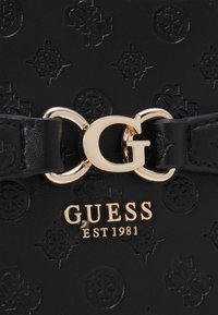 Borsa a tracolla in similpelle nera con motivo impresso, hardware dorato e dettaglio con logo. Presenta una caratteristica chiusura a forma di 'G'.