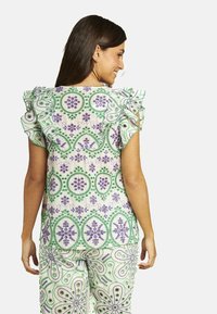 Blusa con estampado floral y mangas acampanadas, en colores verde, púrpura y blanco. La tela es ligera y con textura.