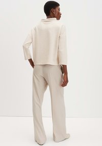 Pullover beige con colletto alto, maniche a tre quarti e vestibilità rilassata, abbinato a pantaloni larghi beige chiaro. Tessuto liscio.