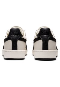Białe i czarne skórzane sneakersy o gładkim wykończeniu. Posiadają zaokrąglony czubek, płaską podeszwę oraz czarne akcenty na pięcie i bokach.