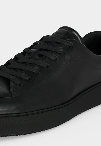 Μαύρο δερμάτινο sneaker χαμηλού προφίλ με μαύρα κορδόνια και χοντρή σόλα, κοντινή λήψη που δείχνει υφή και λείο φινίρισμα.