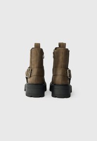 Brown leather ankle boots with a textured finish, featuring a side zipper, buckle detail, and chunky black rubber soles.