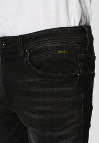 Sorte denimjeans med klassisk fem-lomme-design, diskret falming og guldbranding på forlommerne. Glat tekstur.