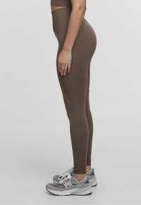 High-waisted brown leggings made from stretch fabric, featuring a smooth texture, form-fitting design, and seamless construction.