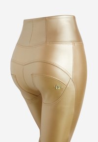 Leggings dorati a vita alta in un materiale lucido e testurizzato, con cuciture curve e un piccolo logo sul taschino posteriore.